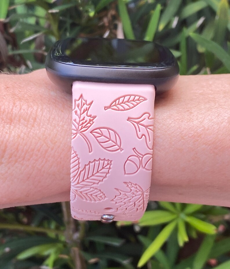 May include: A pink silicone watch band with a leaf and acorn design. The band is compatible with a smartwatch.