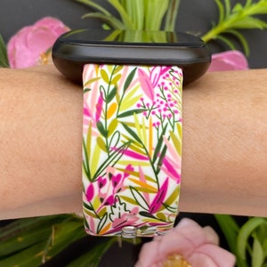 May include: A white watch band with a floral pattern in shades of pink, green, and yellow. The band is made of silicone and has a smooth finish.