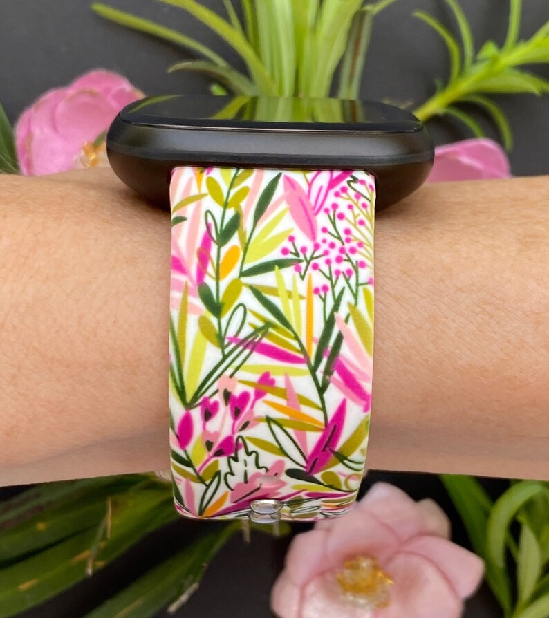 May include: A white watch band with a floral pattern in shades of pink, green, and yellow. The band is made of silicone and has a smooth finish.