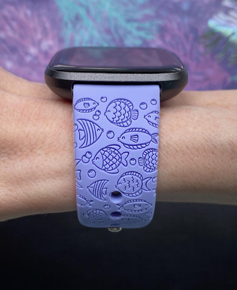 May include: A purple silicone watch strap with a fish pattern. The strap is designed for a smartwatch and has a black watch face.