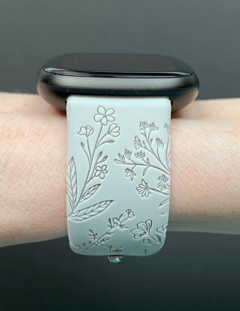 May include: White smartwatch band with a floral design. The band is made of silicone and has a raised floral pattern.