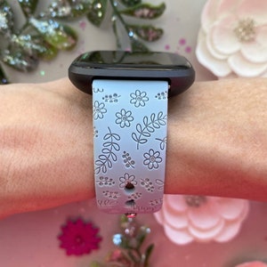 K&ouml;nnte beinhalten: Ein hellblaues Smartwatch-Armband mit Blumenmuster. Das Armband hat einen wei&szlig;en Hintergrund mit grauen Blumen und Bl&auml;ttern.