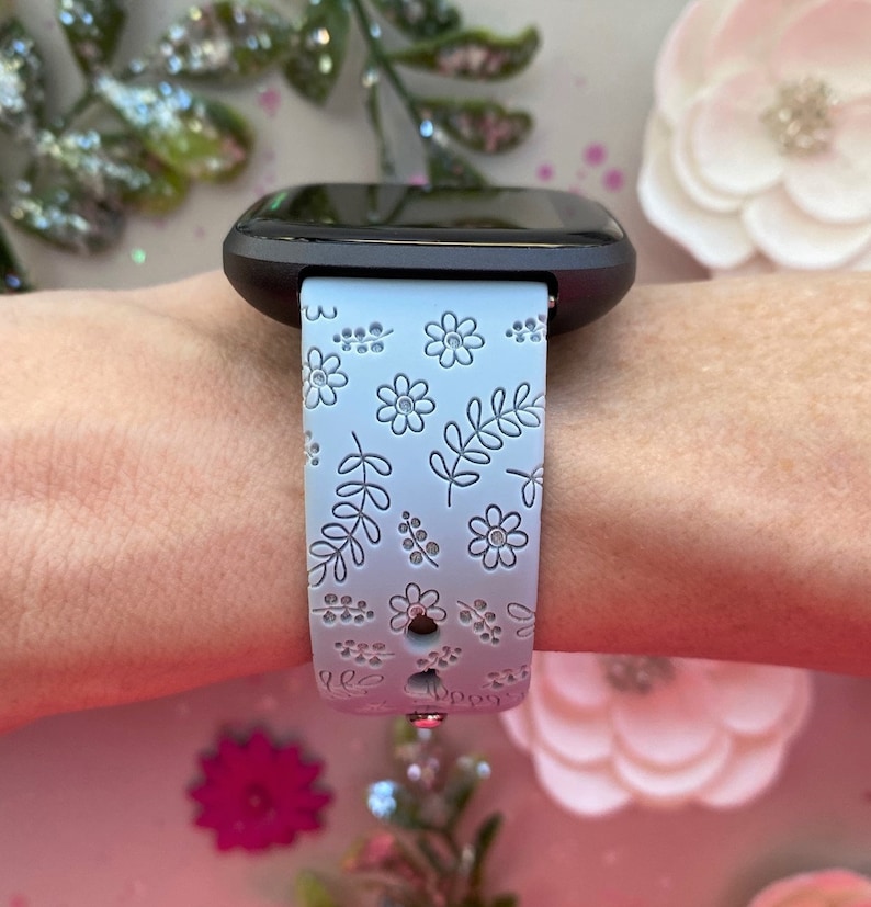 K&ouml;nnte beinhalten: Ein hellblaues Smartwatch-Armband mit Blumenmuster. Das Armband hat einen wei&szlig;en Hintergrund mit grauen Blumen und Bl&auml;ttern.