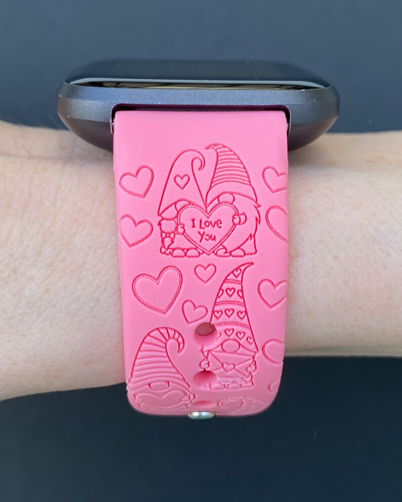 Peut inclure: Bracelet de montre en silicone rose avec un motif de couple de gnomes. Les gnomes tiennent un c&oelig;ur sur lequel est inscrit "Je t'aime". Le bracelet est d&eacute;cor&eacute; de c&oelig;urs.
