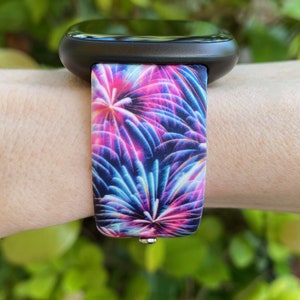 May include: A black smartwatch with a colorful firework print silicone band. The band has a blue, pink, and purple firework design.