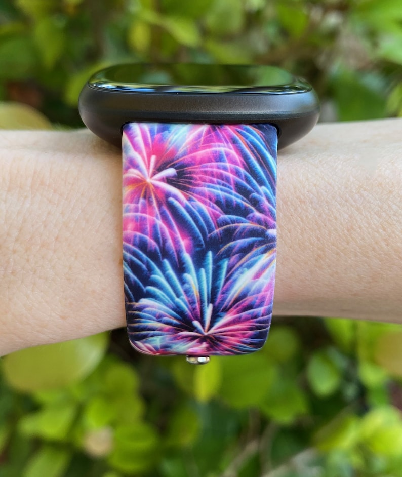May include: A black smartwatch with a colorful firework print silicone band. The band has a blue, pink, and purple firework design.