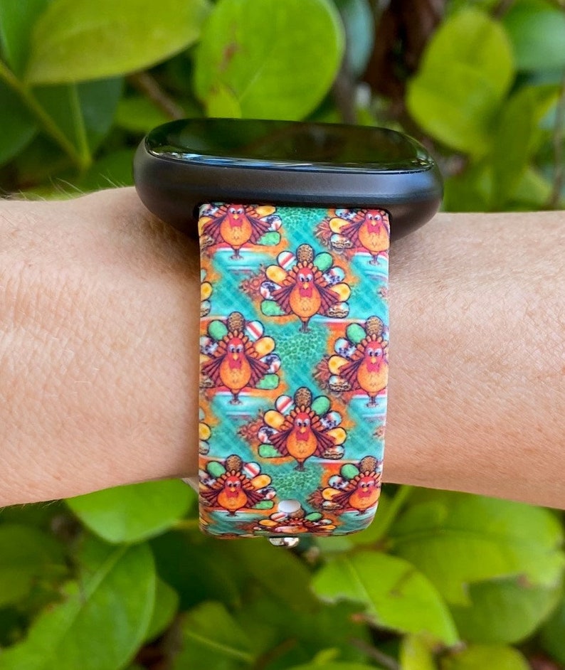 K&ouml;nnte beinhalten: Ein farbenfrohes Armband mit einem Muster aus Truth&auml;hnen und herbstlichen Designs. Das Armband ist aus Silikon und kompatibel mit Smartwatches.
