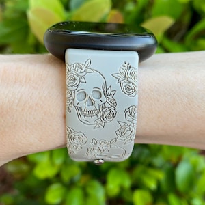 May include: A white silicone watch strap with a skull and roses design. The strap is on a person's wrist.
