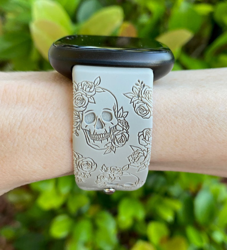 May include: A white silicone watch strap with a skull and roses design. The strap is on a person's wrist.