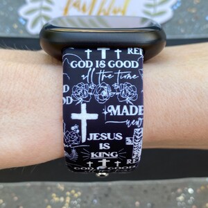 May include: Black and white watch band with a repeating pattern of crosses, flowers, and the text "God is good", "all the time", "Made new", "Jesus is King", and "God is good".