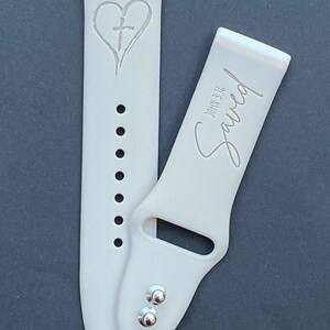 May include: A white silicone watch band with a heart and cross design on one side and the text "Saved" with "John 3:16" on the other side.