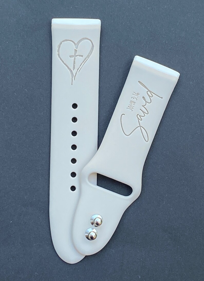 May include: A white silicone watch band with a heart and cross design on one side and the text "Saved" with "John 3:16" on the other side.