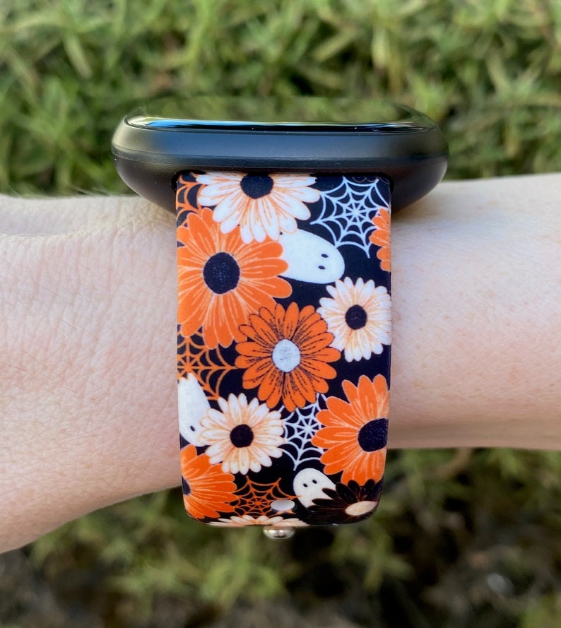 May include: A black smartwatch with a bright orange, white and black patterned band featuring flowers, ghosts and spiderwebs.
