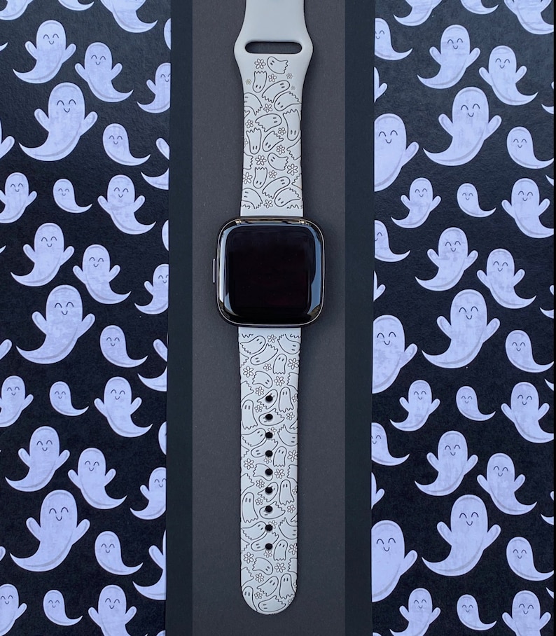 Puede incluir: Una correa de reloj de silicona blanca con un patr&oacute;n de fantasmas y flores. La correa est&aacute; dise&ntilde;ada para un reloj inteligente y tiene una pantalla negra.