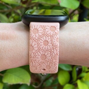 May include: A pink silicone watch band with a floral pattern. The band is designed for a smartwatch with a square face.