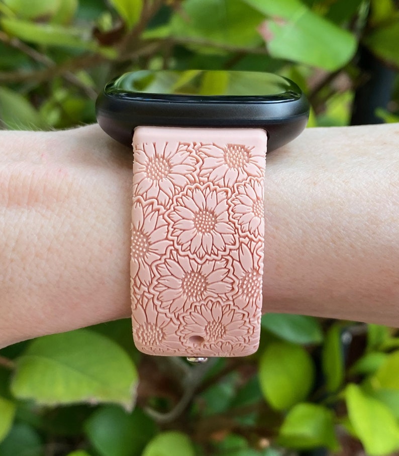 May include: A pink silicone watch band with a floral pattern. The band is designed for a smartwatch with a square face.