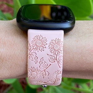 May include: A pink silicone watch band with a floral design featuring white sunflowers and leaves. The band is designed for a smartwatch.