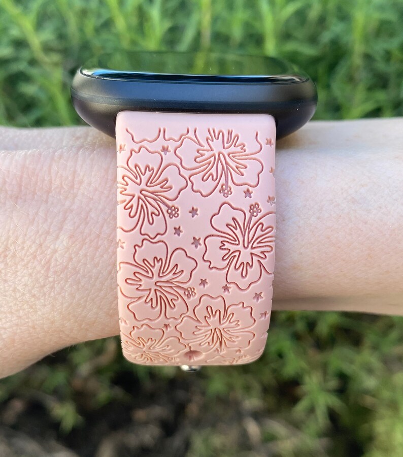 May include: A pink silicone watch band with a hibiscus flower pattern. The band is designed for a smartwatch.