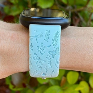 May include: A light blue watch band with a dragonfly and butterfly design. The band is made of silicone and has a smooth finish.
