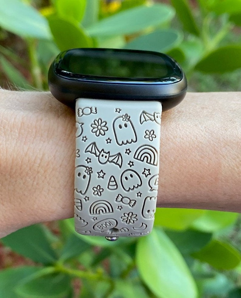 May include: A light gray smartwatch band with a Halloween-themed design. The band features ghosts, bats, stars, rainbows, candy, and the word "BOO!" in a white outline.