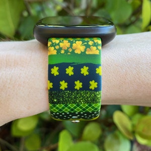 May include: A green, black, and gold watch band with a shamrock pattern. The band is made of silicone and has a sporty look.