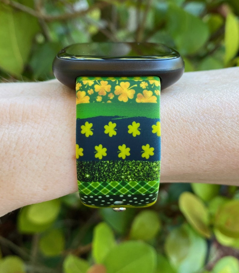 May include: A green, black, and gold watch band with a shamrock pattern. The band is made of silicone and has a sporty look.