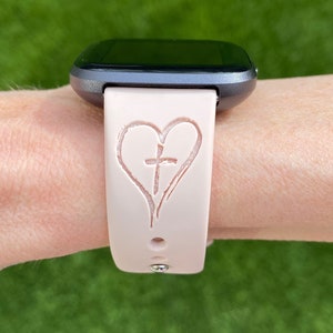 K&ouml;nnte beinhalten: Ein rosafarbenes Silikon-Armband mit einem Herz- und Kreuzdesign.