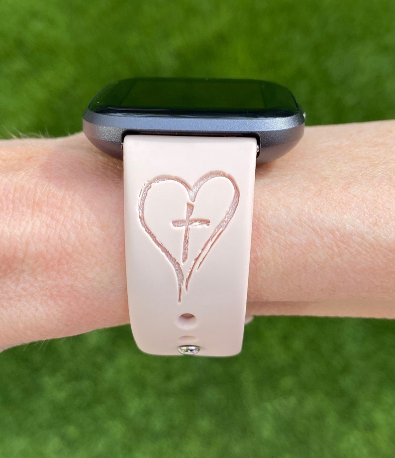 K&ouml;nnte beinhalten: Ein rosafarbenes Silikon-Armband mit einem Herz- und Kreuzdesign.