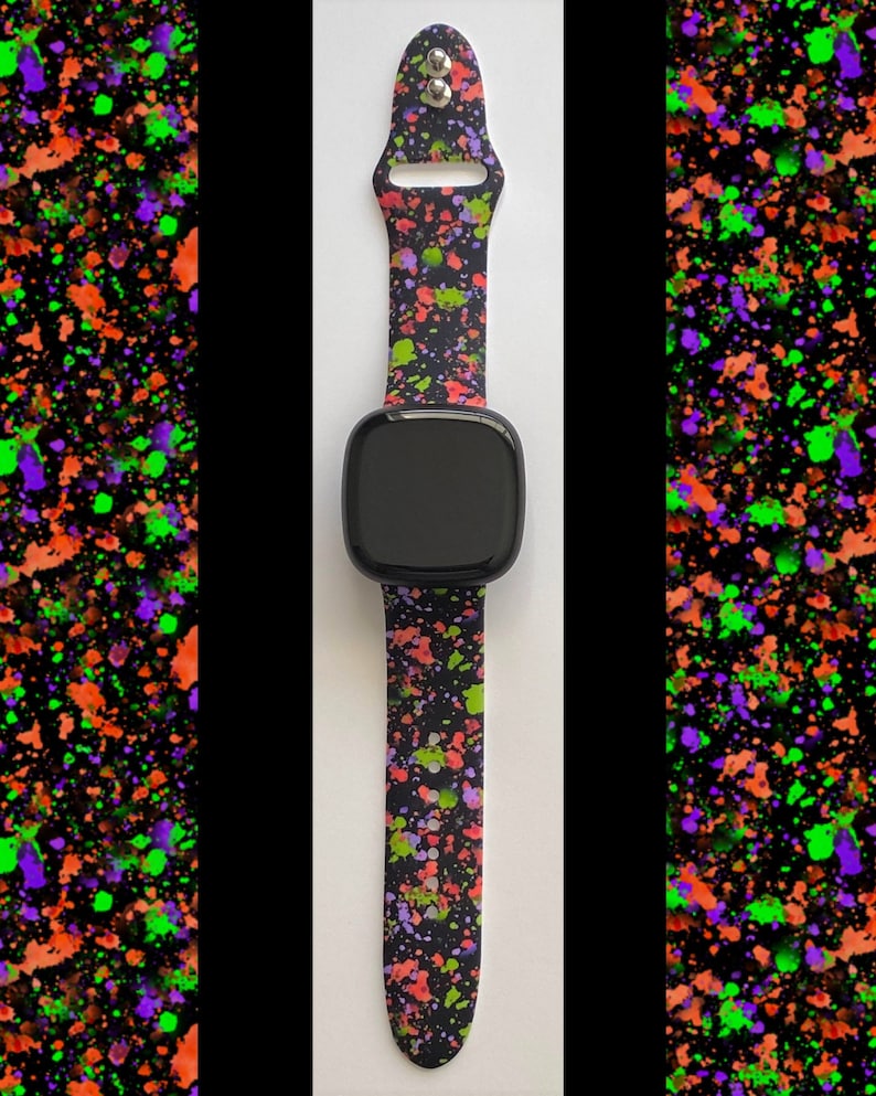 Puede incluir: Una correa de reloj negra con un patr&oacute;n de salpicaduras de pintura verde, naranja y morada. La correa est&aacute; hecha de silicona y tiene una esfera de reloj negra.