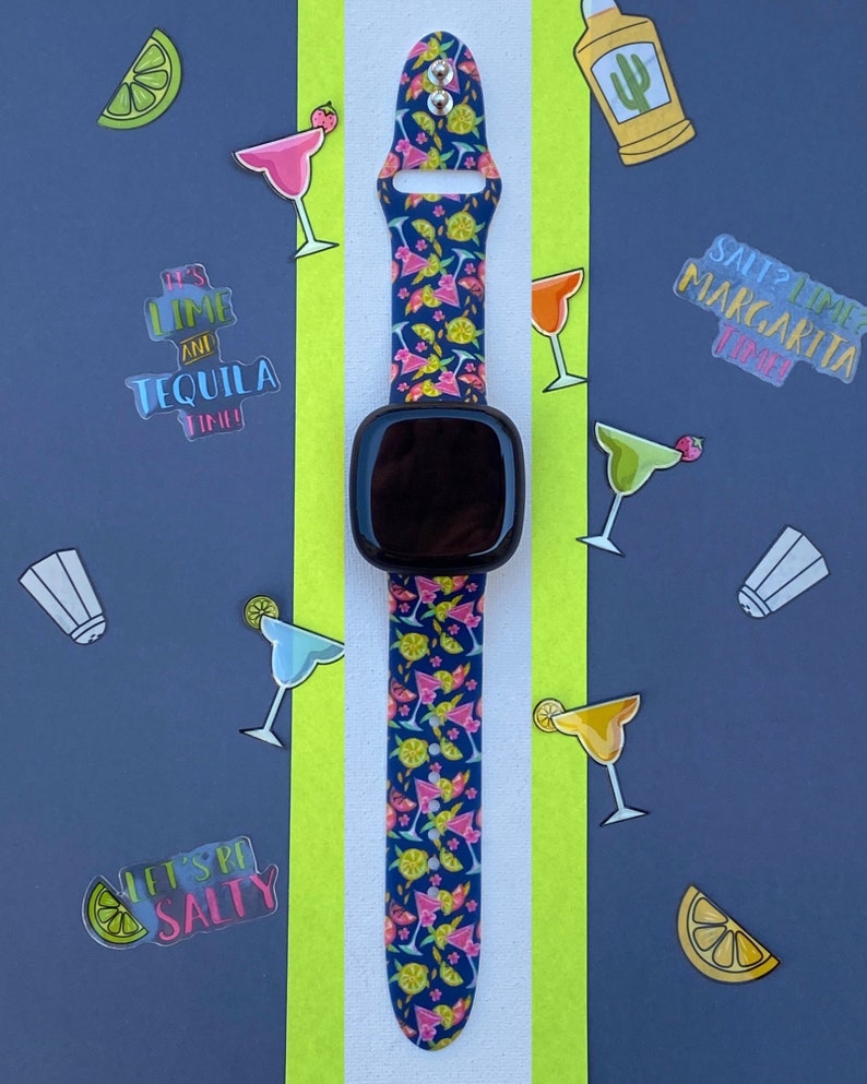 May include: A blue and pink patterned watch band with a black smartwatch face. The band features images of lemons, limes, and cocktails. The background features various stickers with text such as "It's lime and tequila time!" and "Salt? Lime? Margarita Time!"