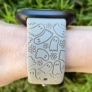 May include: A gray silicone watch band with a pattern of ghosts and flowers. The band is designed for a smartwatch.