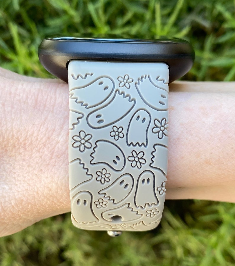 May include: A gray silicone watch band with a pattern of ghosts and flowers. The band is designed for a smartwatch.