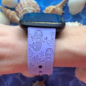 May include: A purple silicone watch band with a mermaid and sea life design. The band features mermaids, starfish, seashells, and a whale.