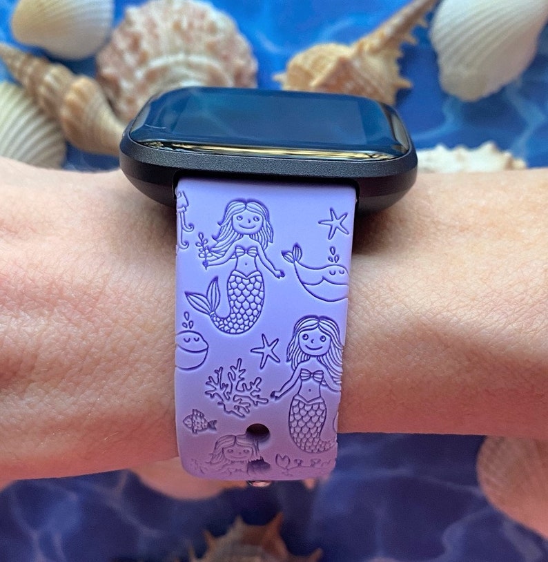 May include: A purple silicone watch band with a mermaid and sea life design. The band features mermaids, starfish, seashells, and a whale.