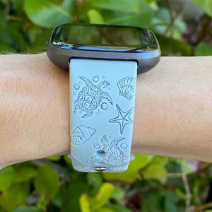May include: A light blue silicone watch band with a sea turtle, seashell, and starfish design. The band is compatible with a smartwatch.