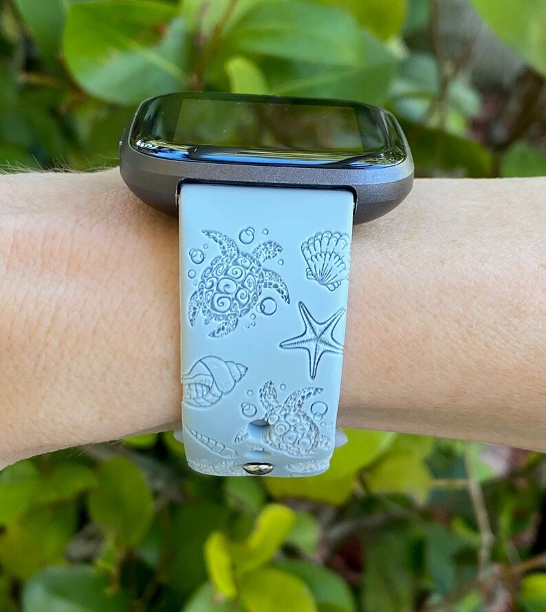 May include: A light blue silicone watch band with a sea turtle, seashell, and starfish design. The band is compatible with a smartwatch.