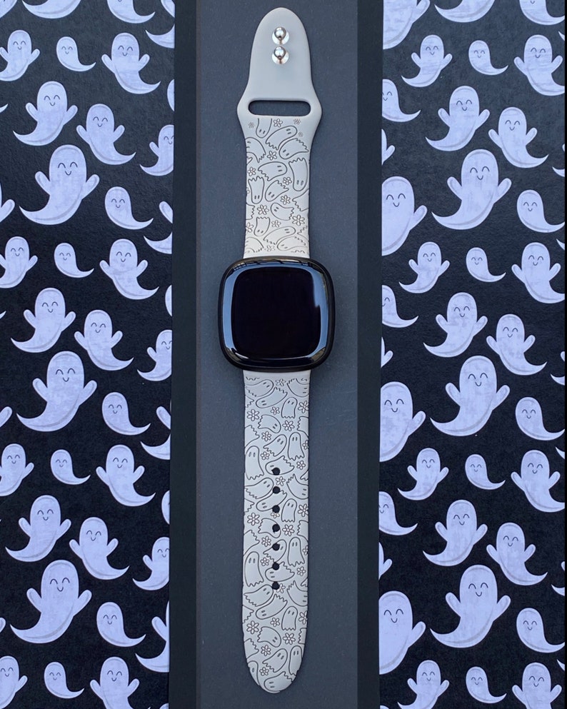 May include: A white silicone watch band with a ghost pattern. The band is designed for a smartwatch with a black face.