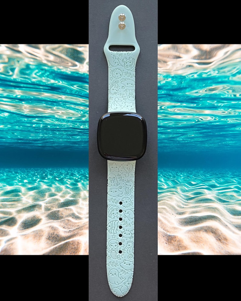 May include: A light blue smartwatch band with a black square watch face. The band is decorated with a repeating pattern of sea creatures. The band is made of a soft, flexible material.