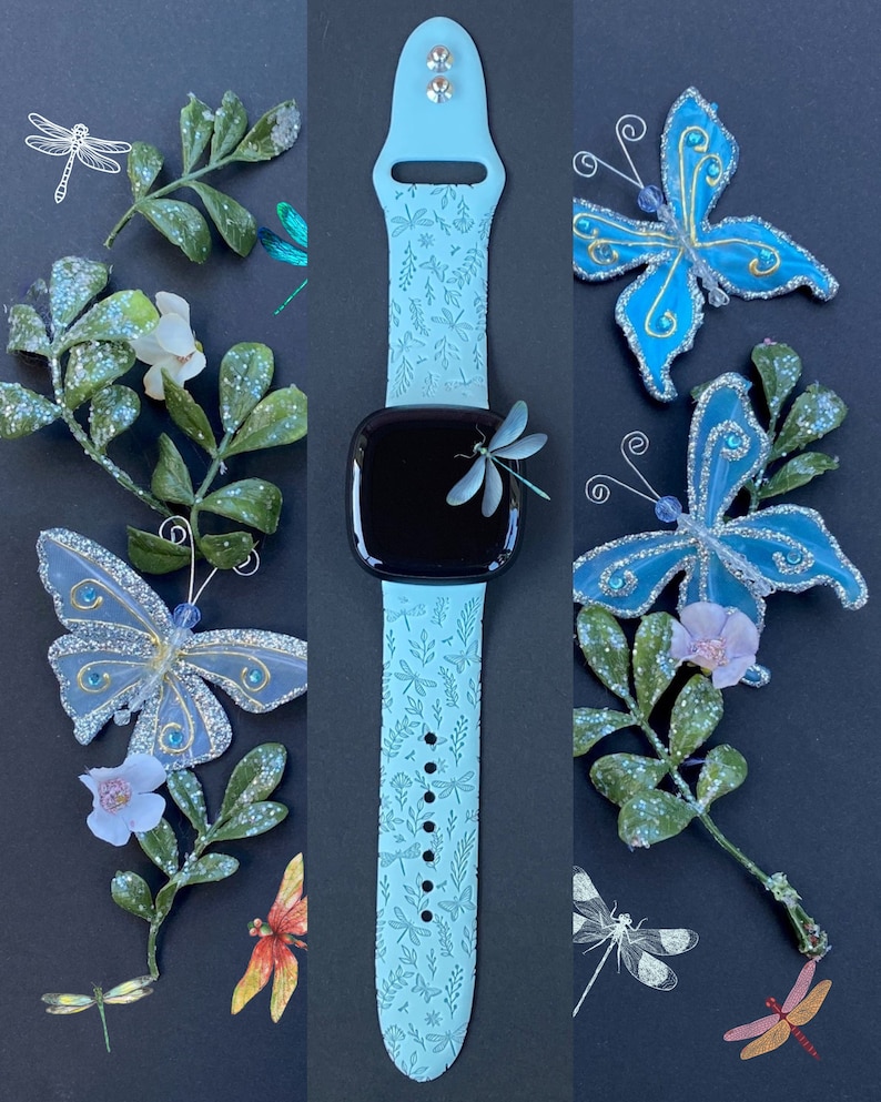 May include: A light blue silicone watch band with a dragonfly and leaf pattern. The band is designed for an Apple Watch and has a black watch face with a dragonfly on it.