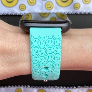 May include: A turquoise smartwatch band with a repeating pattern of smiley faces. The band is made of silicone and has a smooth, matte finish.