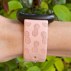 May include: A pink silicone watch band with a pineapple pattern. The band is designed for a smartwatch with a black face.