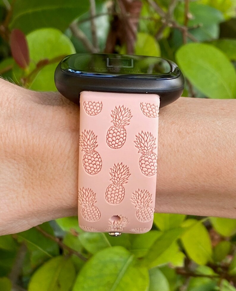 May include: A pink silicone watch band with a pineapple pattern. The band is designed for a smartwatch with a black face.
