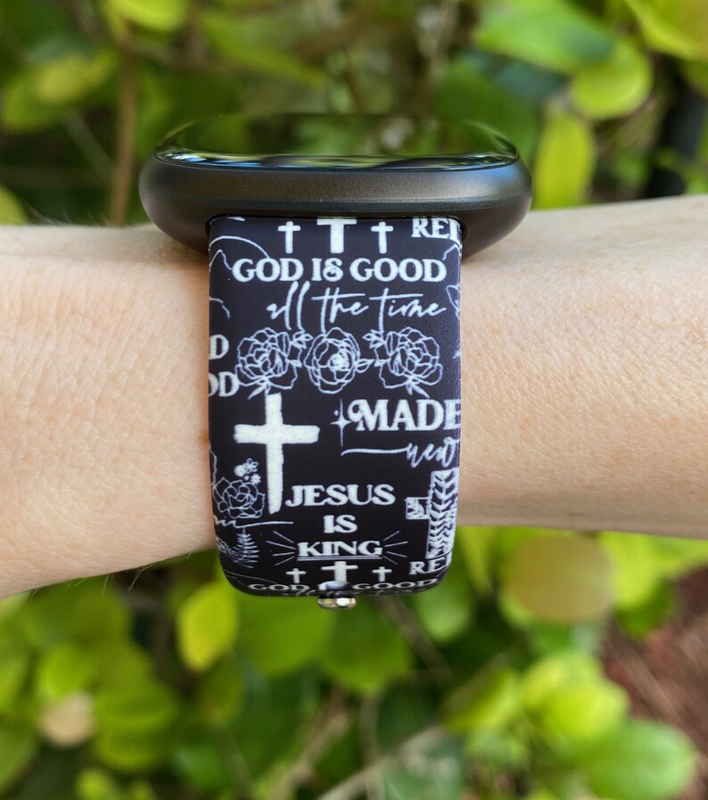May include: Black and white watch band with a repeating pattern of crosses, flowers, and the text "God is good", "Made new", "Jesus is King", and "God is good".