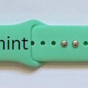 K&ouml;nnte beinhalten: Hellgr&uuml;nes Armband mit wei&szlig;en Akzenten. Das Armband tr&auml;gt den schwarzen Schriftzug "Spearmint". Es hat drei L&ouml;cher und zwei silberfarbene Metallverschl&uuml;sse.