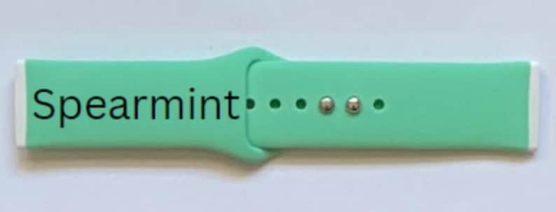 K&ouml;nnte beinhalten: Hellgr&uuml;nes Armband mit wei&szlig;en Akzenten. Das Armband tr&auml;gt den schwarzen Schriftzug "Spearmint". Es hat drei L&ouml;cher und zwei silberfarbene Metallverschl&uuml;sse.