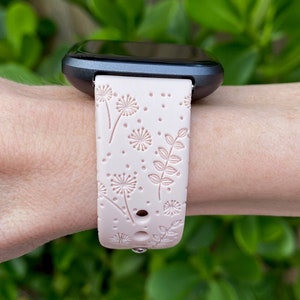 May include: A pink silicone watch band with a floral pattern featuring dandelions and leaves. The band is designed for a smartwatch with a black face.