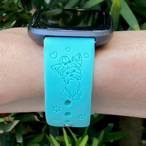 May include: A turquoise blue silicone watch band with a small, white, embossed Yorkshire Terrier design and paw prints. The band is compatible with a smartwatch.