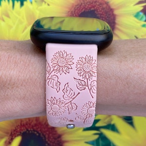 May include: A pink silicone watch band with a sunflower pattern. The band is designed for a smartwatch with a black face.