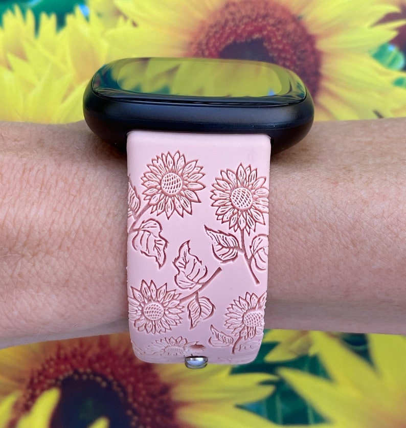 May include: A pink silicone watch band with a sunflower pattern. The band is designed for a smartwatch with a black face.