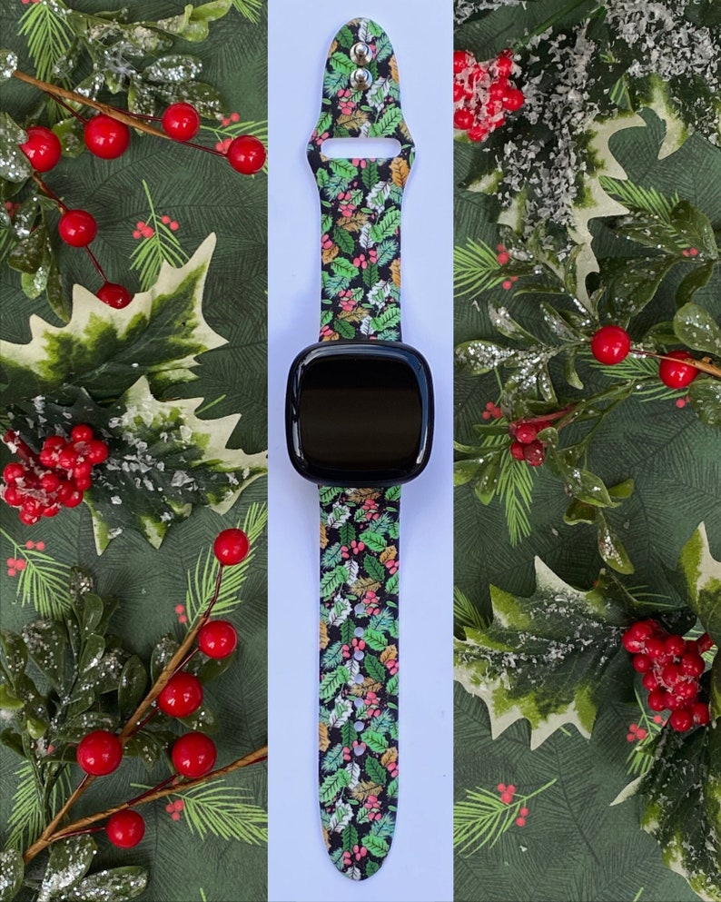 May include: A black smartwatch with a green, red and white festive band. The band features a pattern of holly leaves and berries.